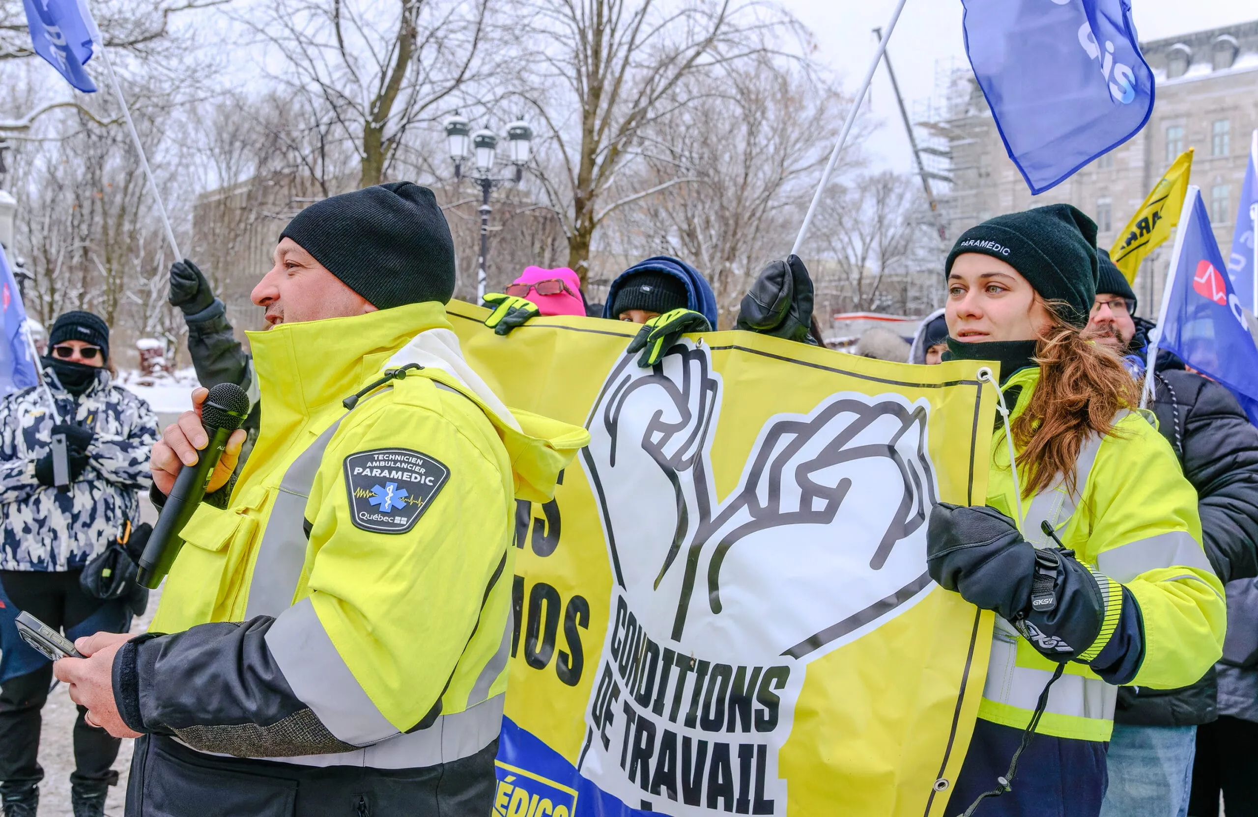 Des paramédics en manifestation tiennent une bannière jaune où l’on lit « Conditions de travail ».
