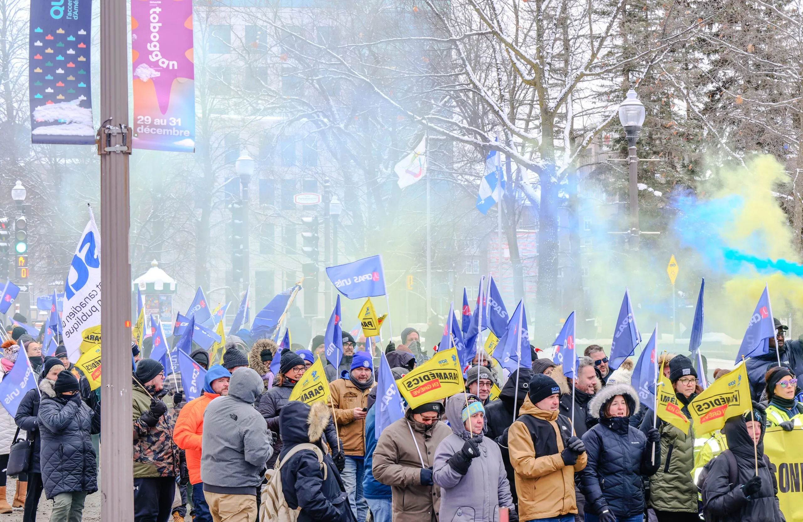 Une foule de manifestants brandit des drapeaux bleus et jaunes dans une rue enneigée, sous des fumigènes.