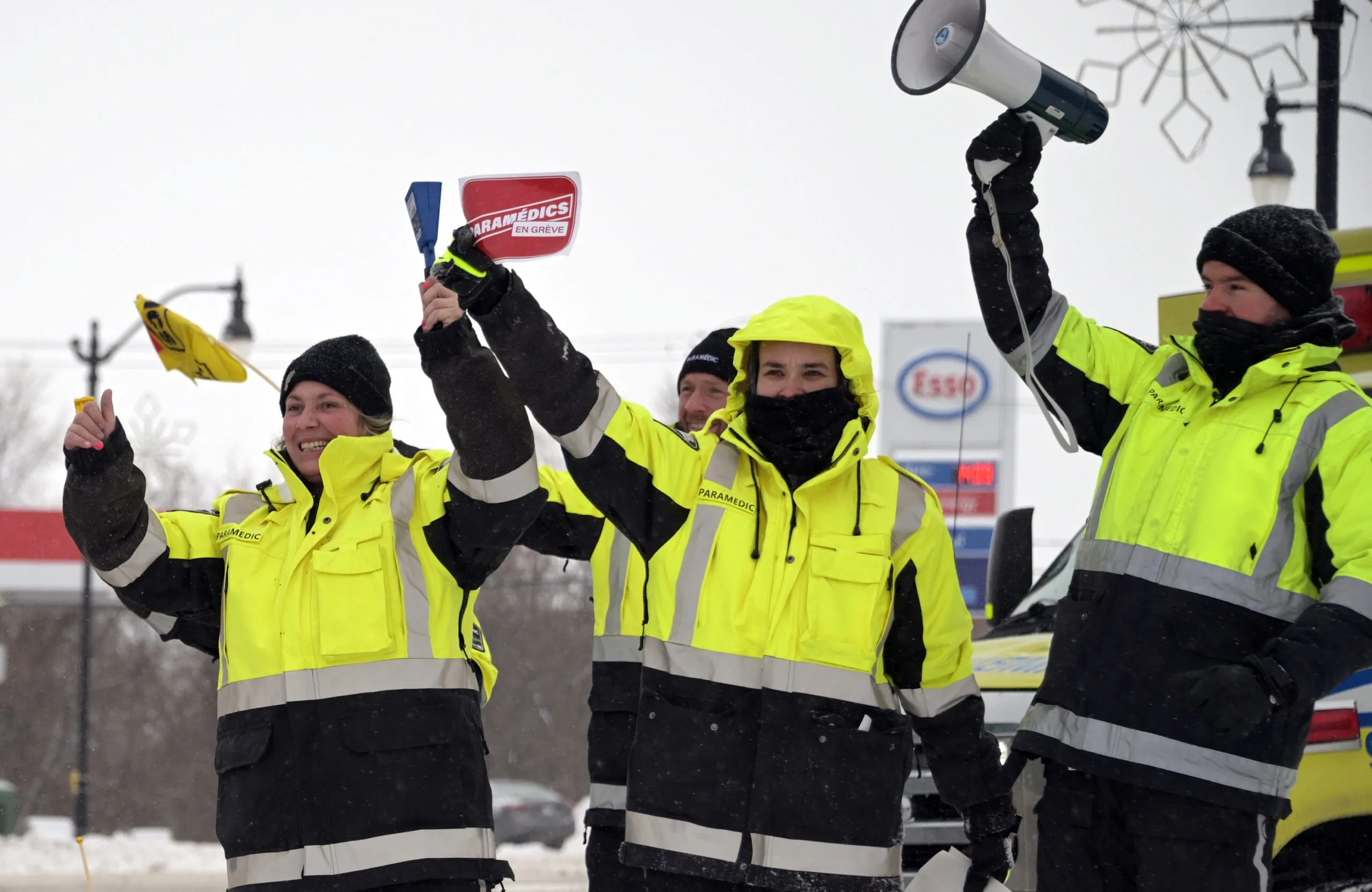 Des paramédics en uniforme jaune lèvent le poing ; l’un d’eux brandit un porte-voix.